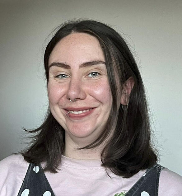 Helena is a white woman with straight brown hair to her shoulders, she is smiling, she has a nose ring and a lip ring.