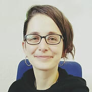 Helena is a white woman with straight brown hair to her shoulders, she is smiling, she has a nose ring and a lip ring.